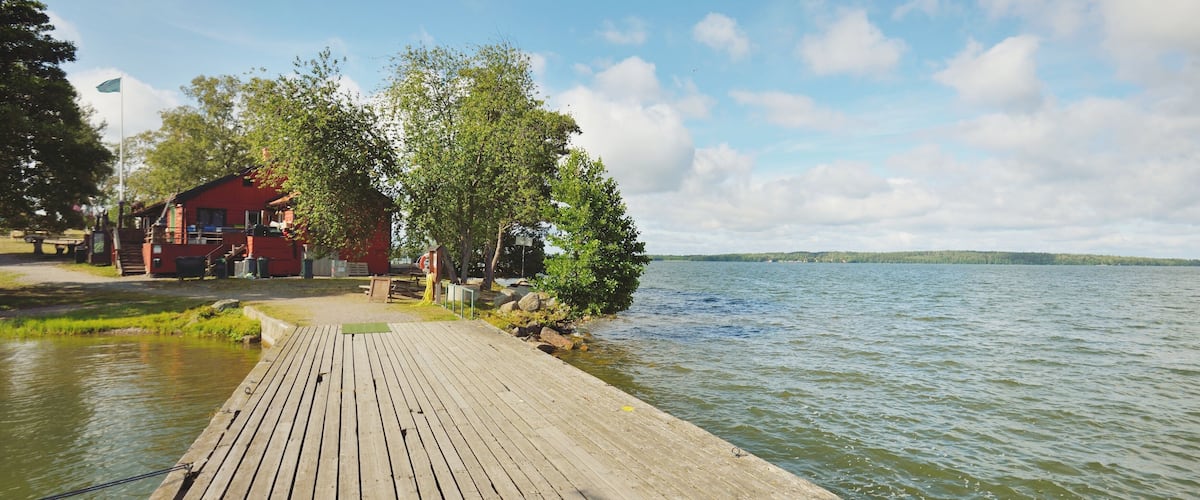 Wooden pier for yachts. Traditional house colored with falu red dye. Summer vacations, recreation, leisure activity, service, private vessels. Björkö island, lake Mälaren, Sweden