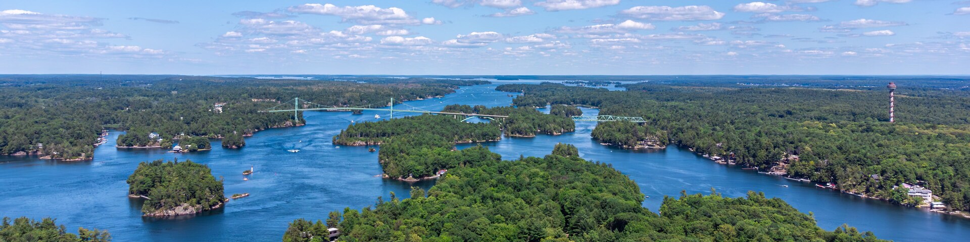 Aerial view of the Saint Lawrence River, Thousand Islands Bridge and 1000 Islands Tower, capturing lush green islands, blue water, and the Canada–US international border on summer day (July 2021)