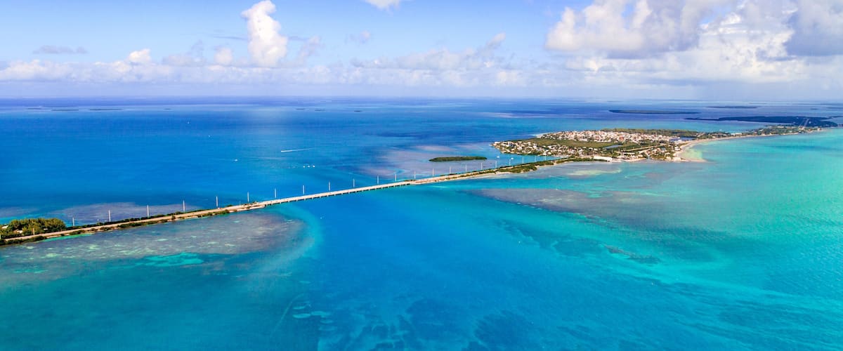A coastal landscape with clear turquoise waters, a long bridge, and a small island with buildings.