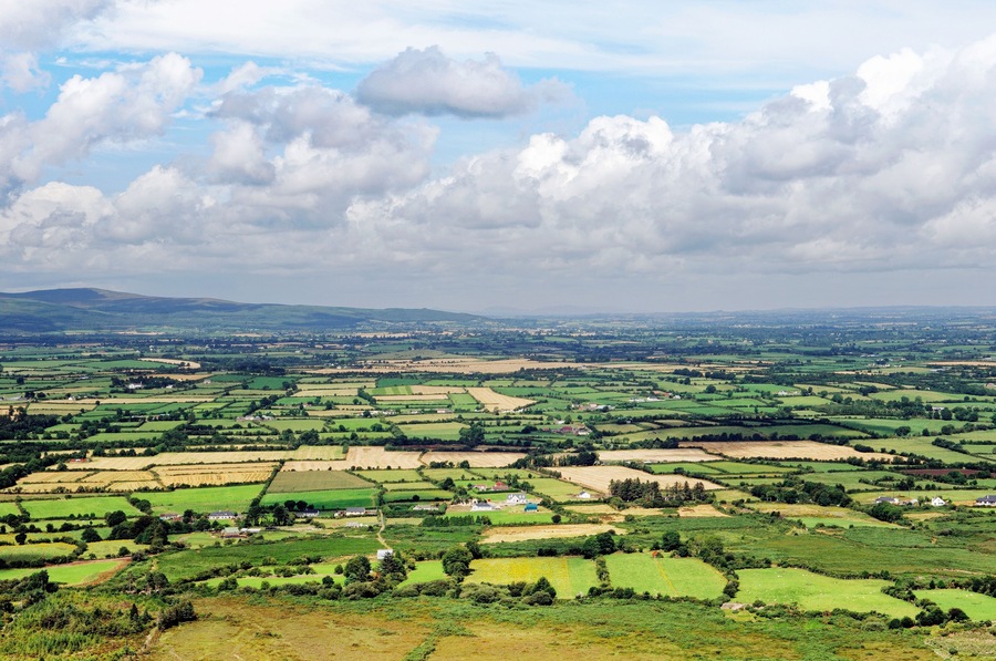 A panoramic view of a rural landscape with rolling hills, fields, and scattered houses.