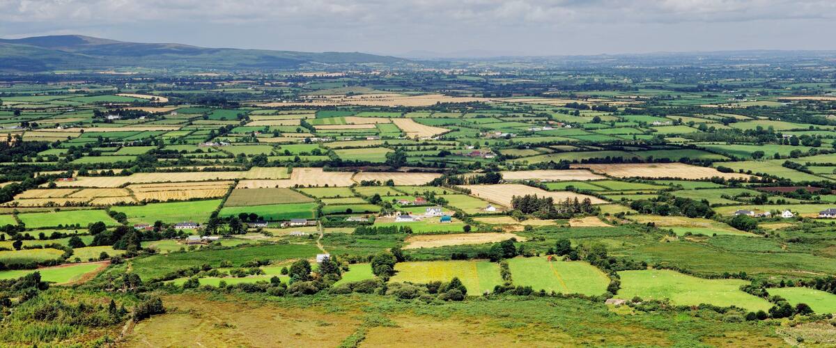 A panoramic view of a rural landscape with rolling hills, fields, and scattered houses.