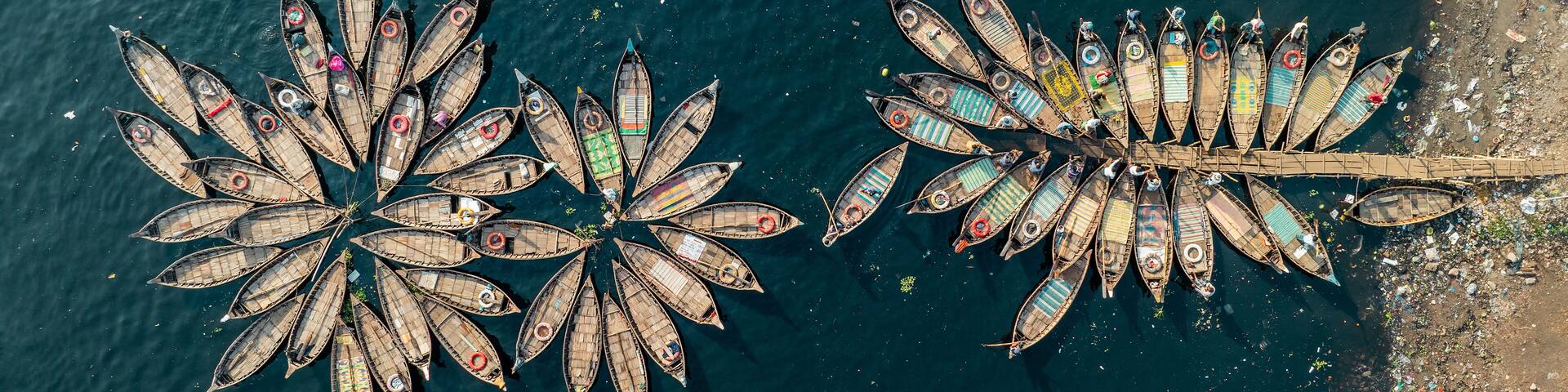 Aerial view of boats clustered together creating a vibrant mosaic on the dark waters, contrasting with the textured shoreline, Dhaka, Dhaka District, Bangladesh.