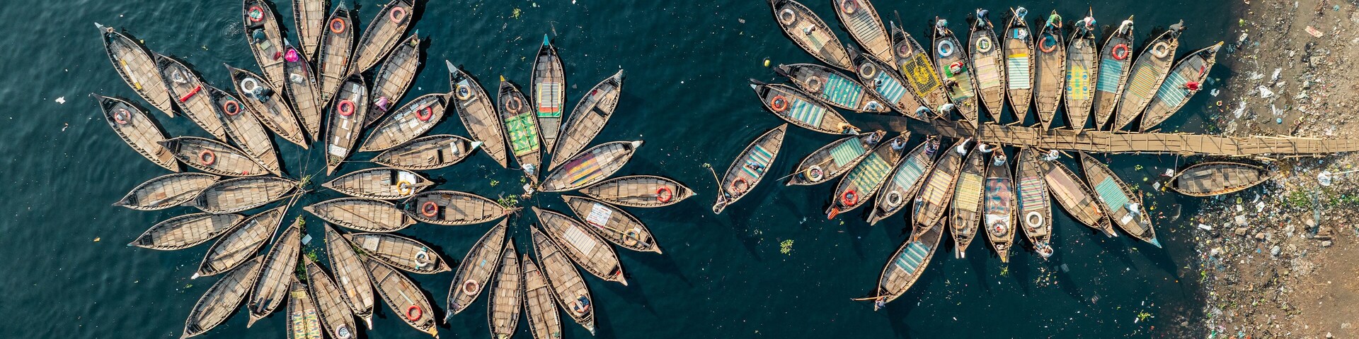 Aerial view of boats clustered together creating a vibrant mosaic on the dark waters, contrasting with the textured shoreline, Dhaka, Dhaka District, Bangladesh.