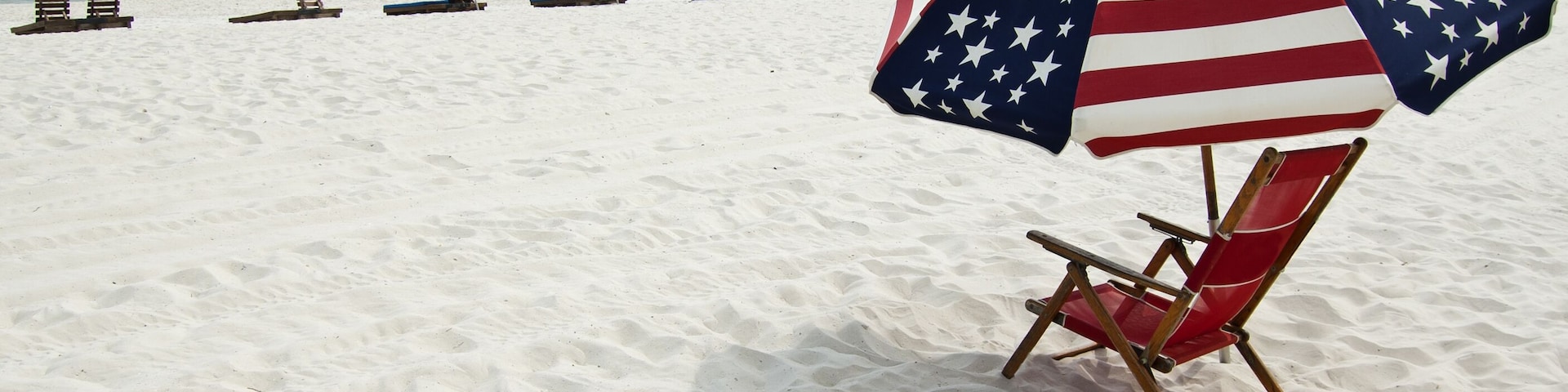 Uma praia com areia branca e uma fileira de cadeiras e guarda-sóis de praia.