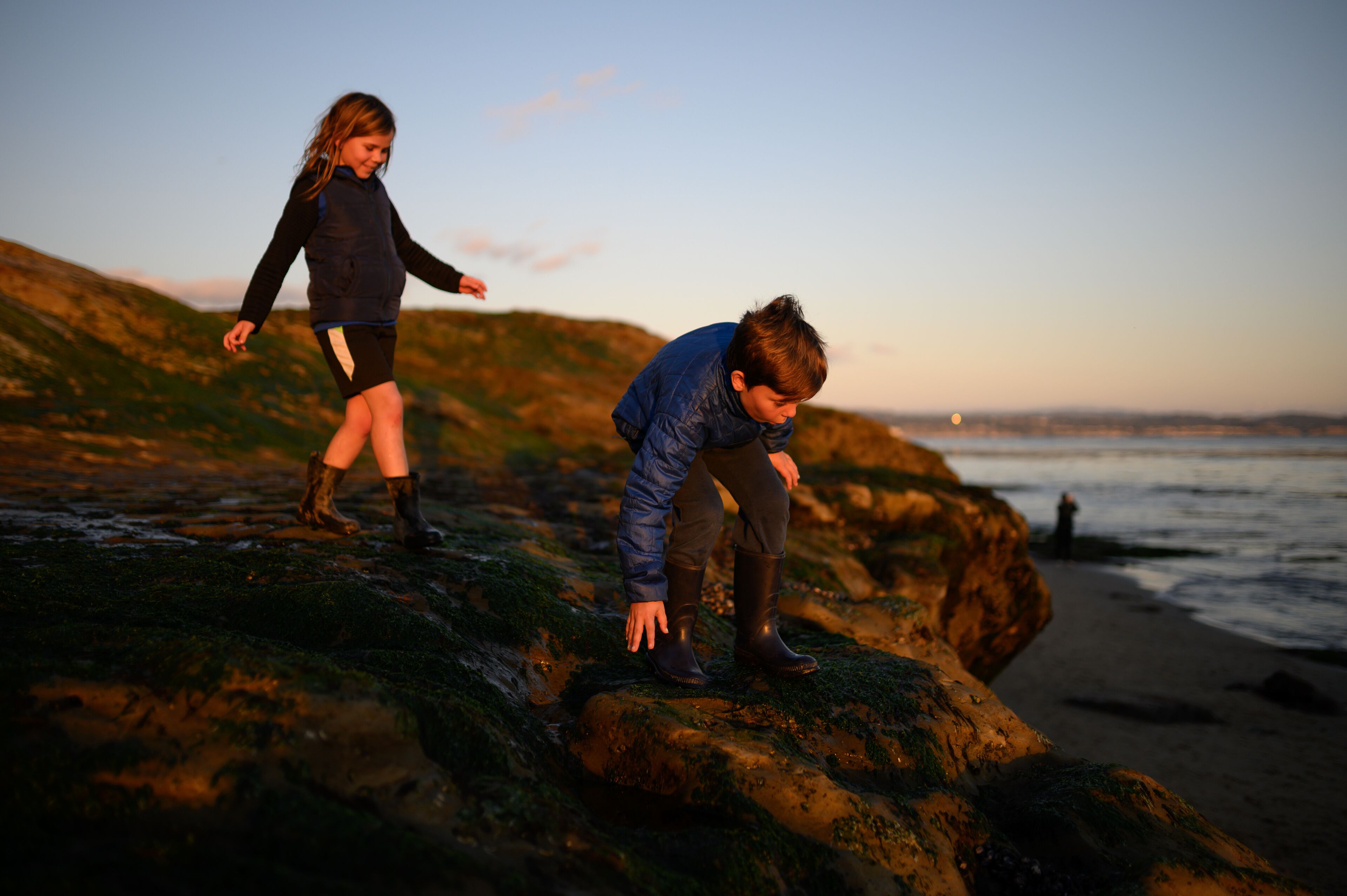 Happy siblings climbing on rocks at sunset near the ocean