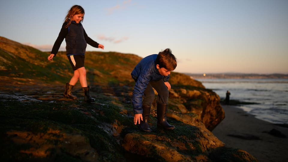 Happy siblings climbing on rocks at sunset near the ocean