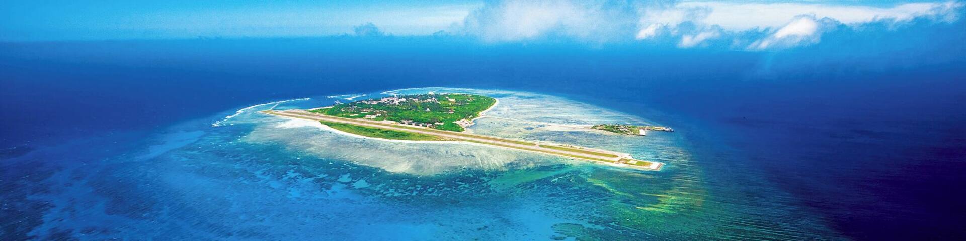 An aerial view of a tropical island with clear blue waters, a runway, and lush greenery.