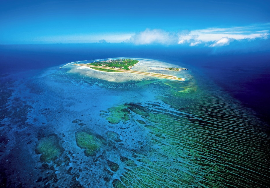 An aerial view of a tropical island with clear blue waters, a runway, and lush greenery.