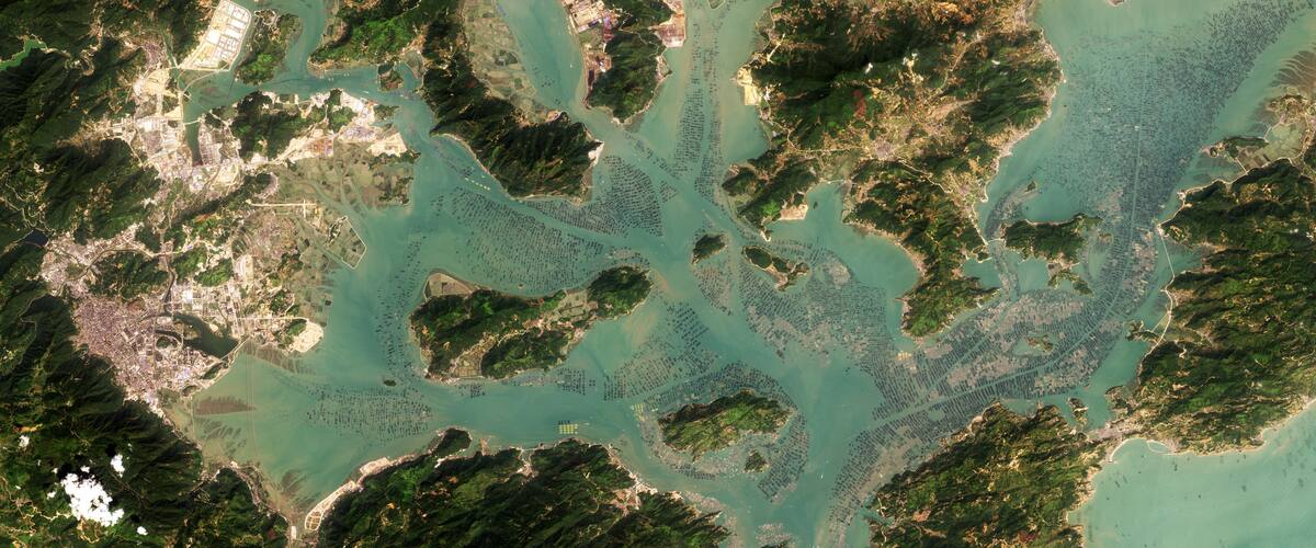 A satellite view of a coastal region with multiple islands, dense green vegetation, and clear turquoise waters.