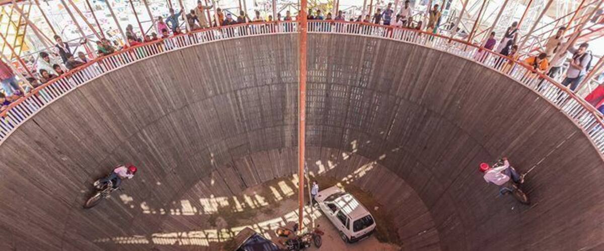 A large circular structure with people riding motorcycles and cars inside.