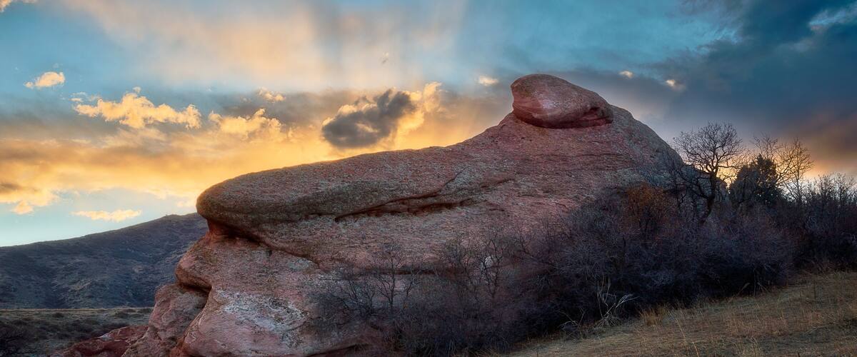 A large rock formation resembling a face in a natural landscape with a sunset sky.