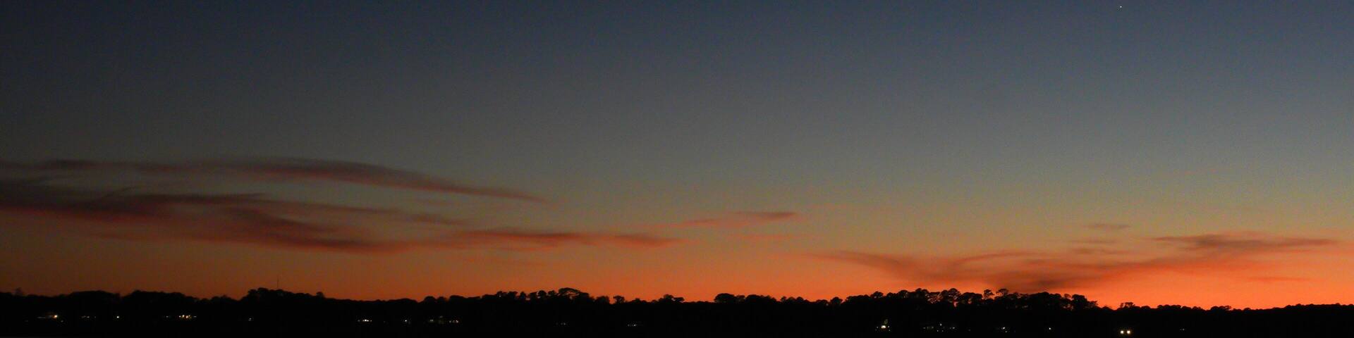 A crescent moon rises over a river in the low country of South Carolina with the marsh and a boat dock in silhouette; copy space; blue hour; twilight