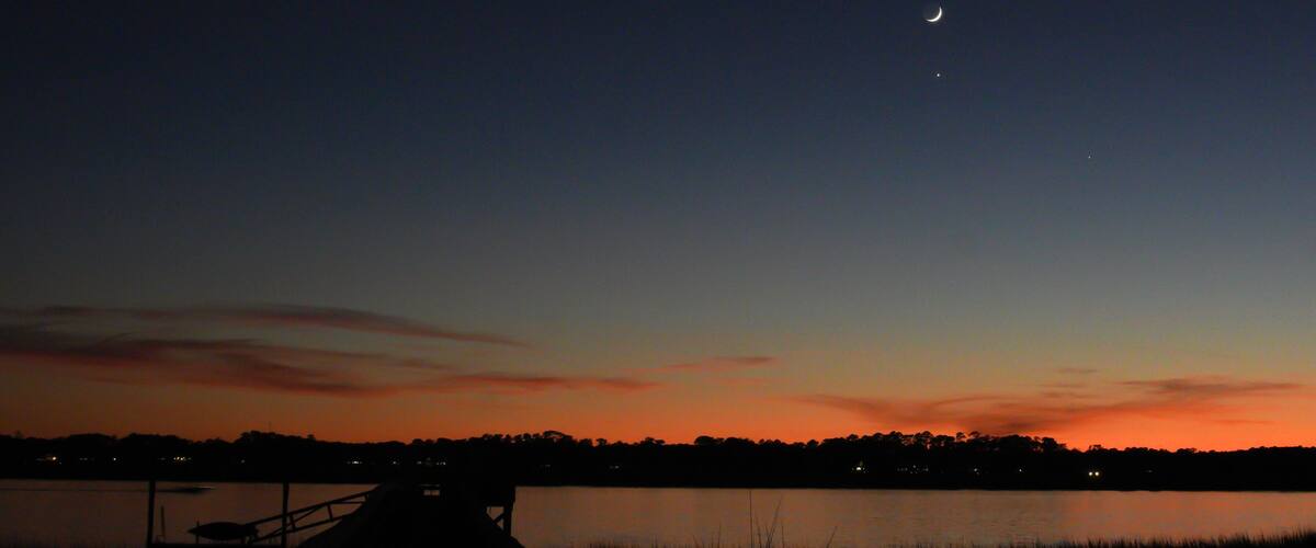 A sunset over a lake with a dock and distant trees silhouetted against the sky.