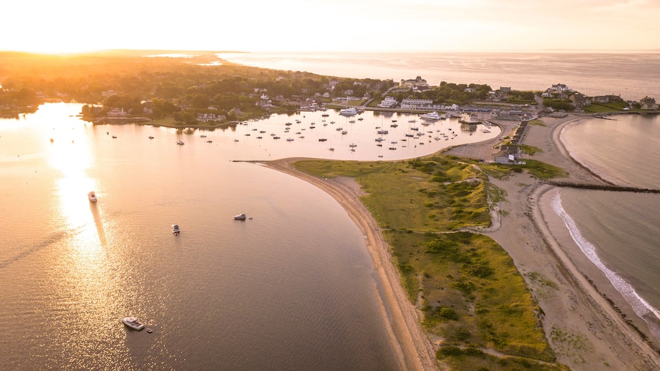 A coastal town with a marina, boats, and a sandy beach during sunset.