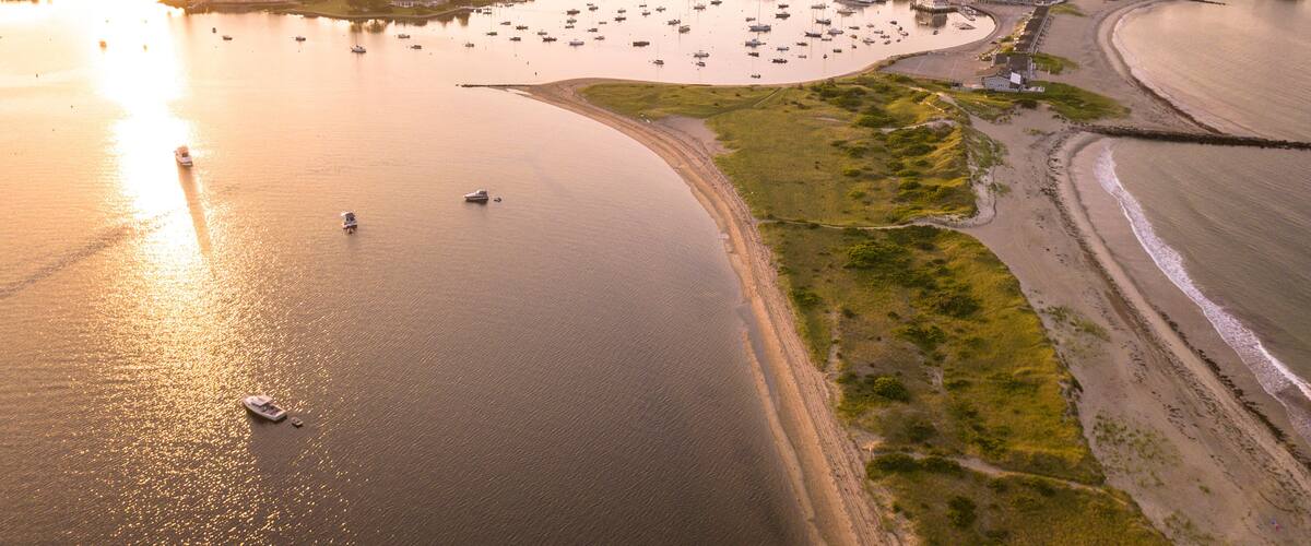 A coastal town with a marina, boats, and a sandy beach during sunset.