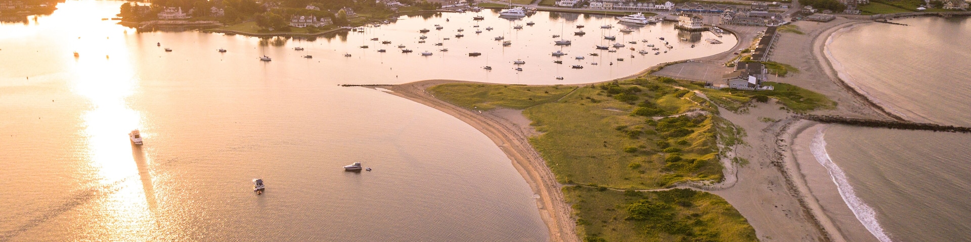 A coastal town with a marina, boats, and a sandy beach during sunset.