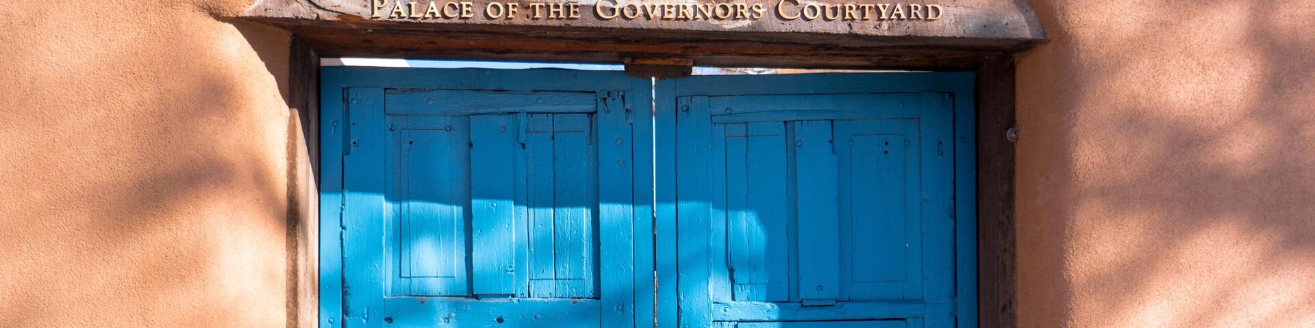 A blue wooden door with a sign above it that reads 'Palace of the Governors Courtyard.'
