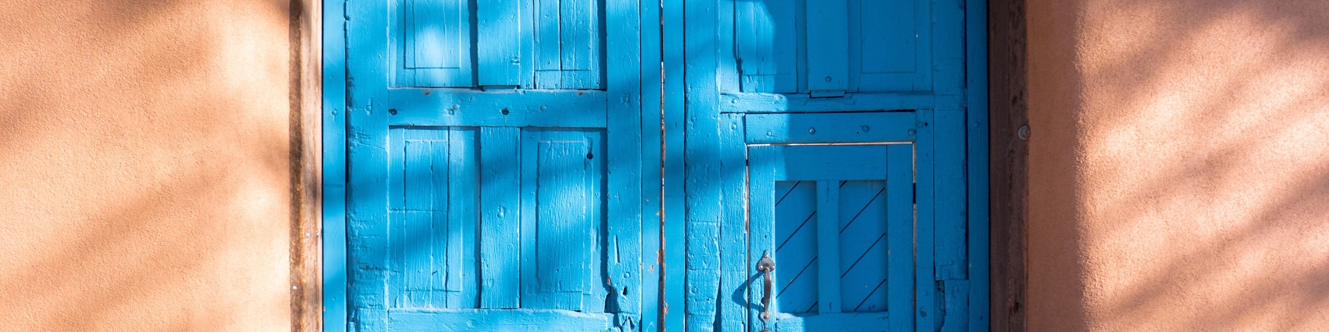 The royal blue wooden doors, adobe walls, and sign over the entrance to the Palace of the Governors Courtyard in Old Town Santa Fe, New Mexico