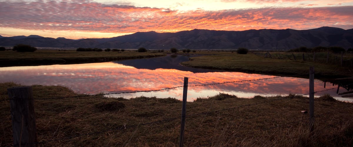 A sunset over a lake with mountains in the background and a barbed wire fence in the foreground.