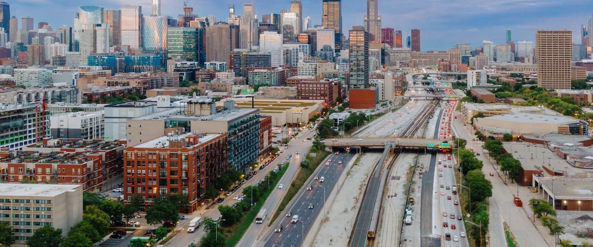 Chicago skyline at twilight, showing city streets, highways, and train tracks. Traffic flows through the urban landscape. West Loop, Chicago, Illinois, United States Of America