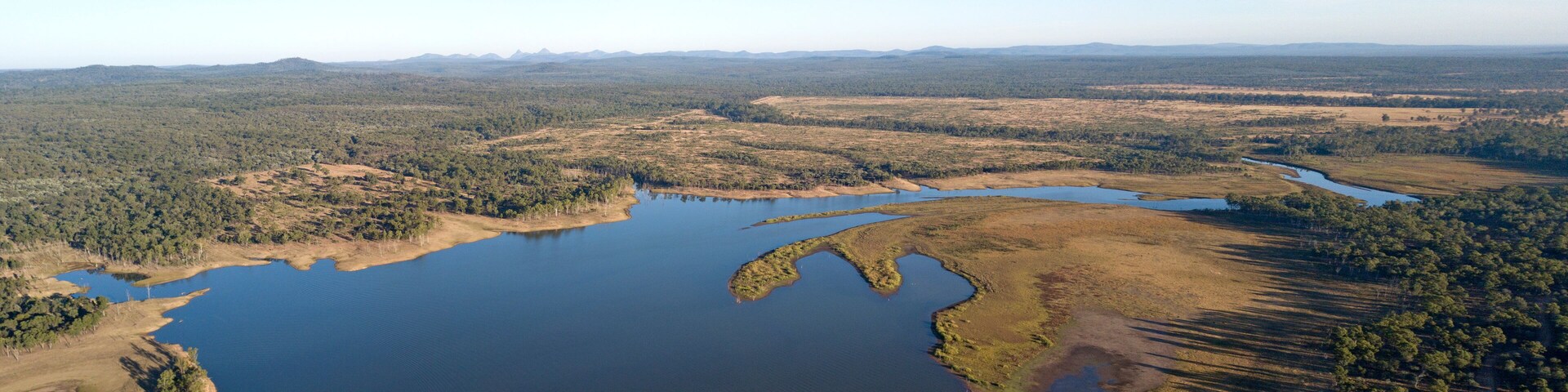 An aerial view of a large lake surrounded by forested areas and distant mountains.