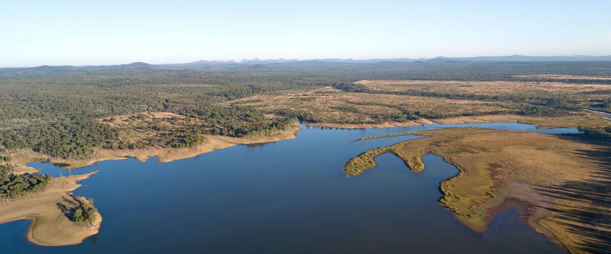 An aerial view of a large lake surrounded by forested areas and distant mountains.