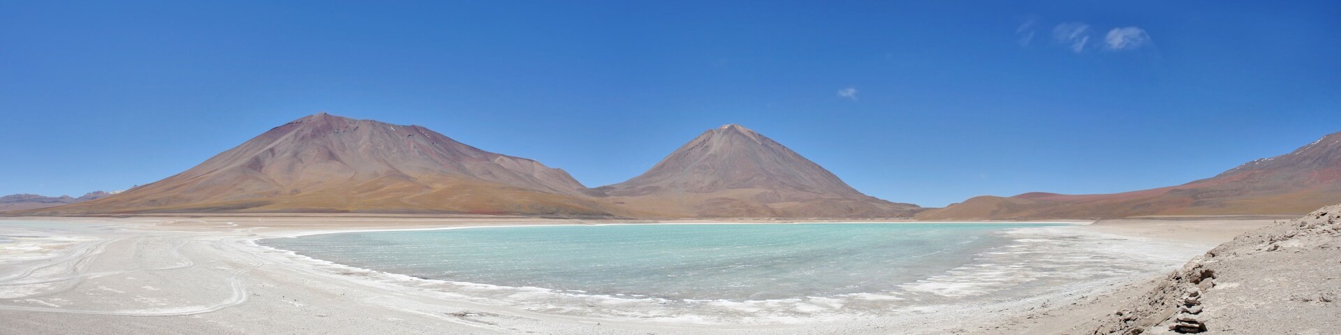 Uma planície salina com duas montanhas imponentes ao fundo e um lago azul-turquesa em primeiro plano.