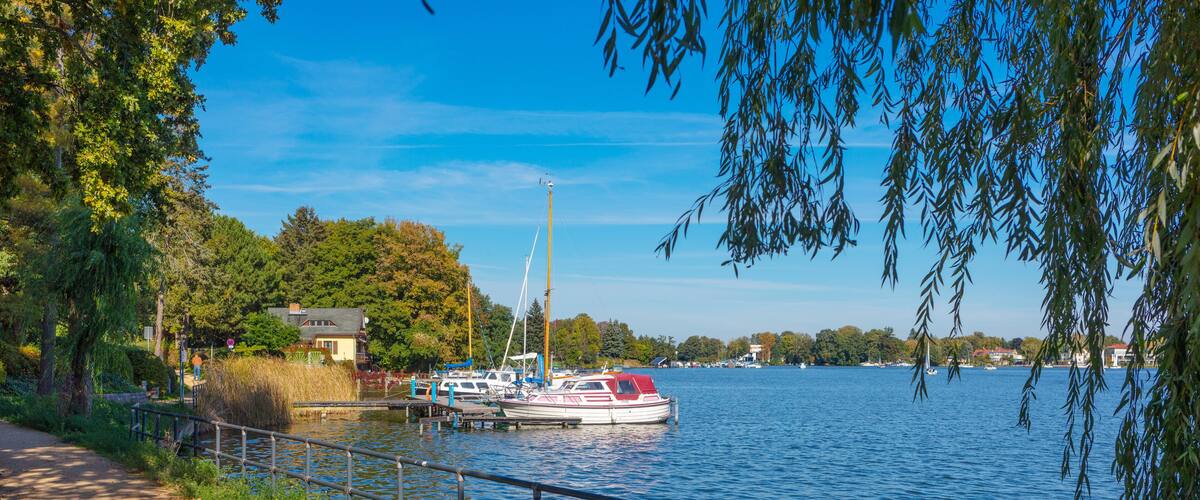 A calm lake with a boat docked near the shore, surrounded by trees and a pathway.