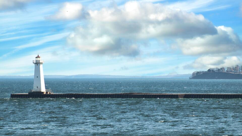 A lighthouse on a pier extending into the water, with a cloudy sky above.