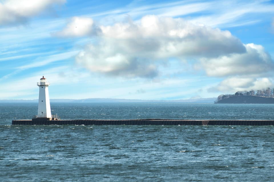 A lighthouse on a pier extending into the water, with a cloudy sky above.