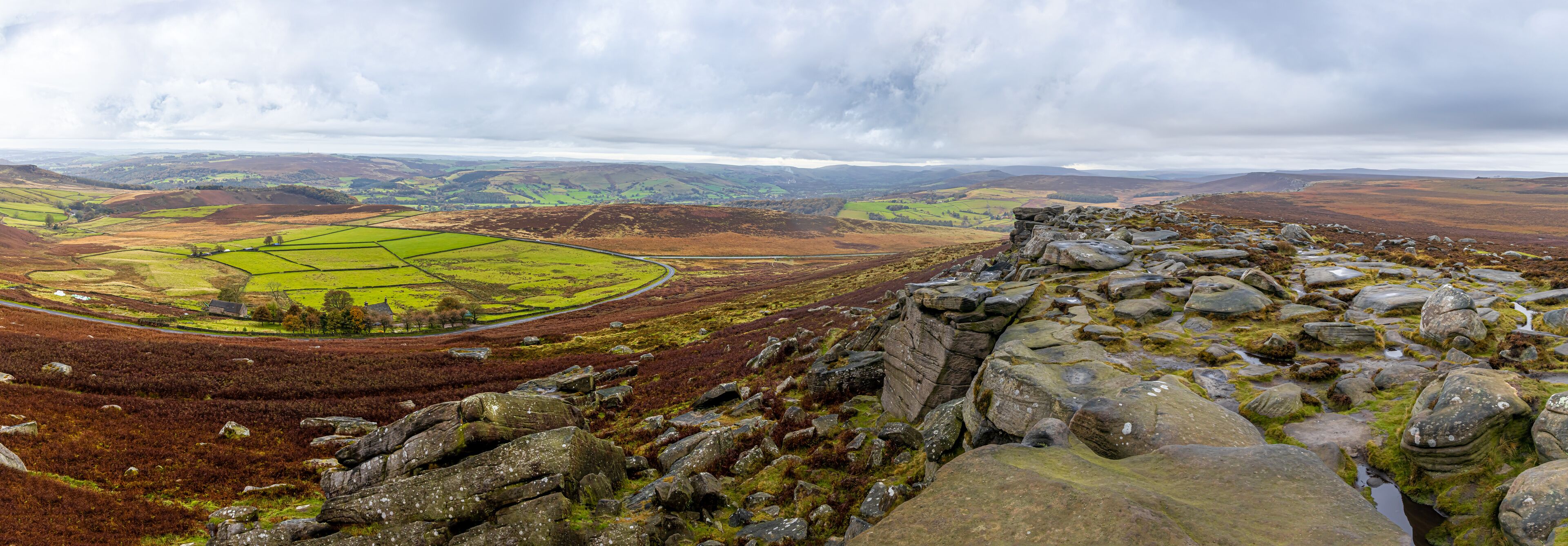 A mountainous landscape with a stone ruin in the foreground and a green valley with fields in the background.