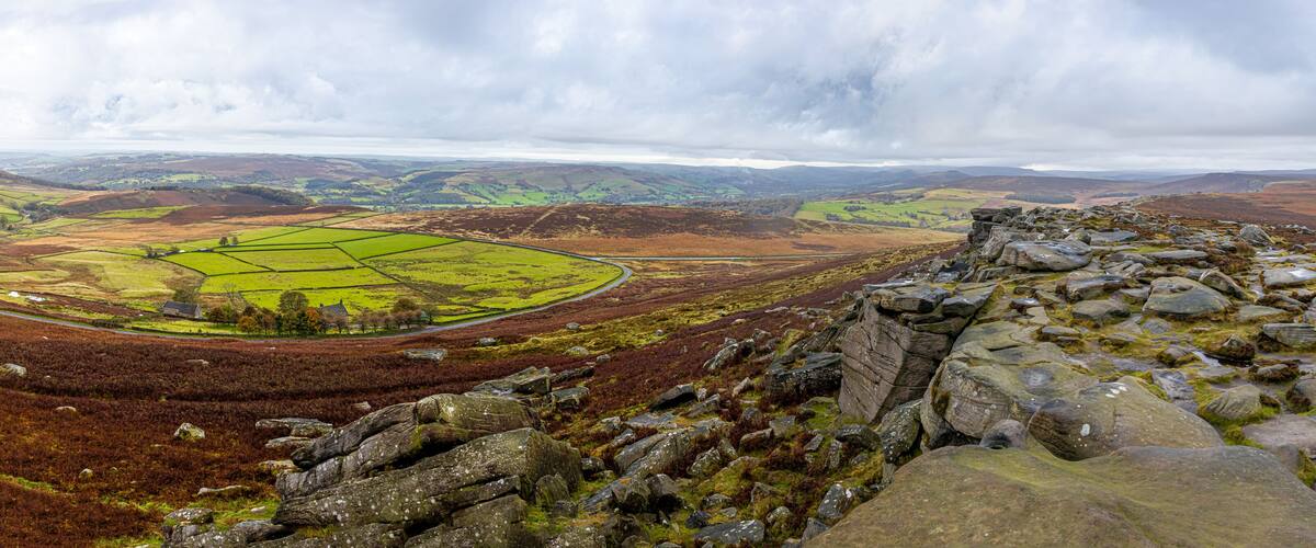 A mountainous landscape with a stone ruin in the foreground and a green valley with fields in the background.