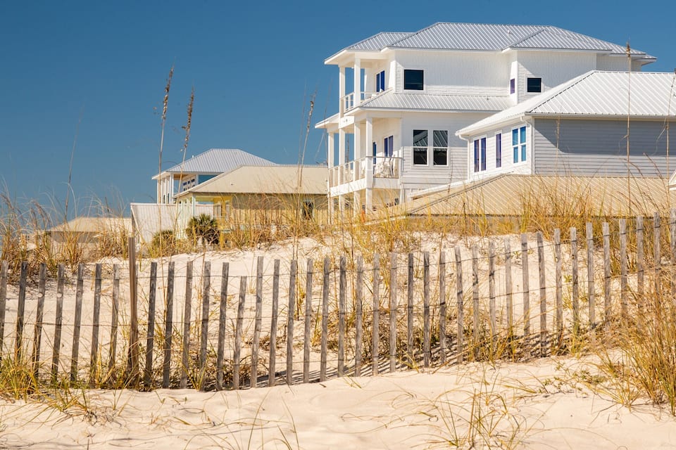 A beachfront house with a sandy beach and a wooden fence.