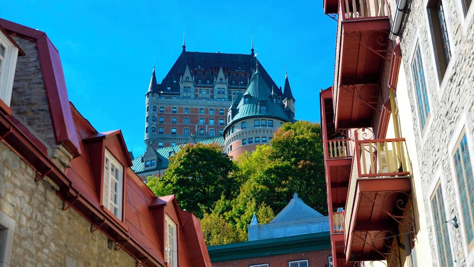 A historic building with a green roof and multiple spires, surrounded by trees and other buildings with red and white facades.