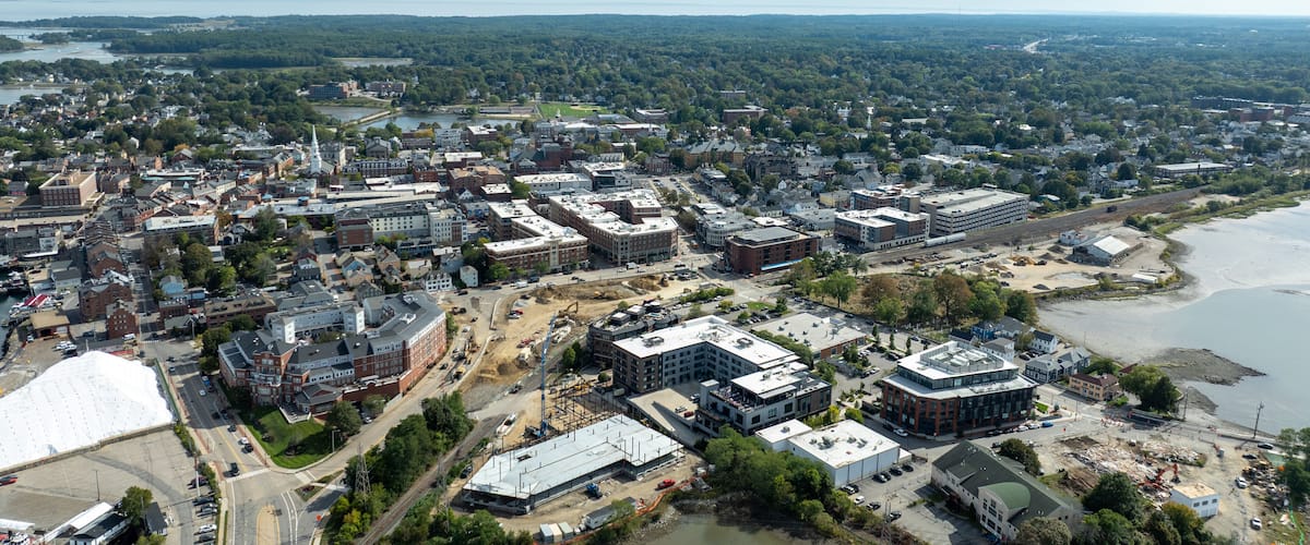 An aerial view of a city with a river, a bridge, and a large construction site.