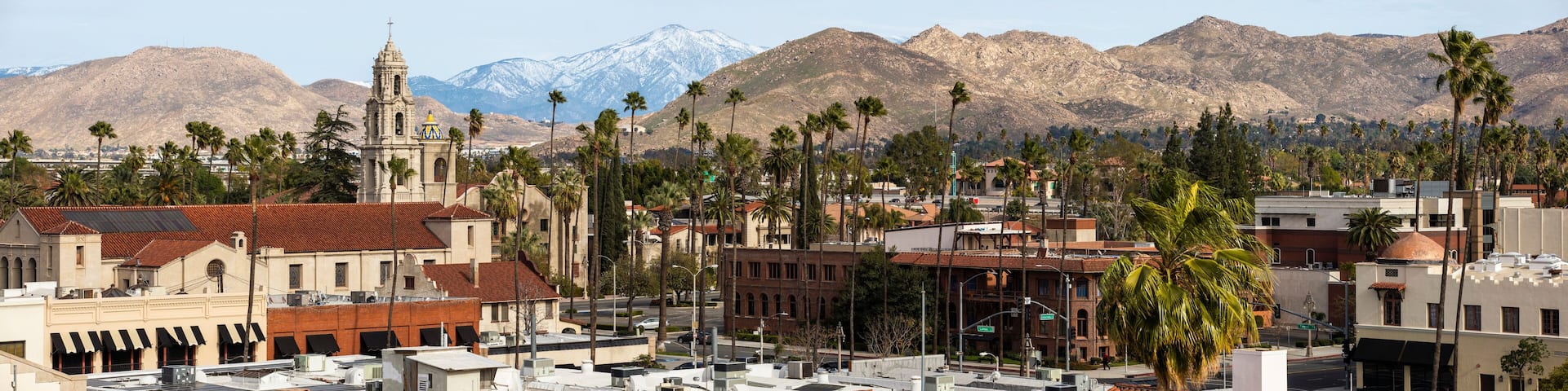 A cityscape with a prominent church, palm trees, and snow-capped mountains in the background.