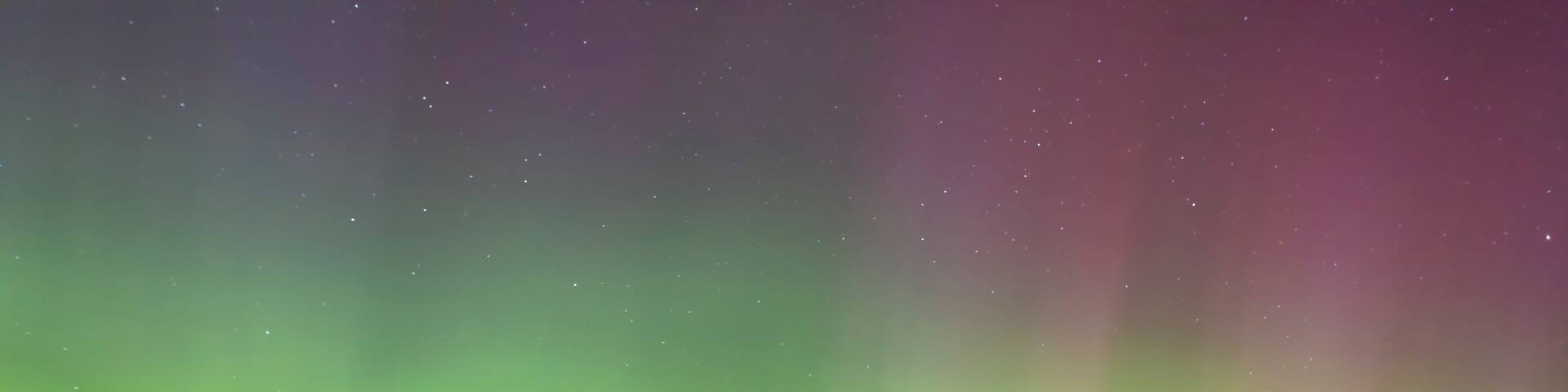 A night scene with the Northern Lights over a calm body of water, a dock, and trees.