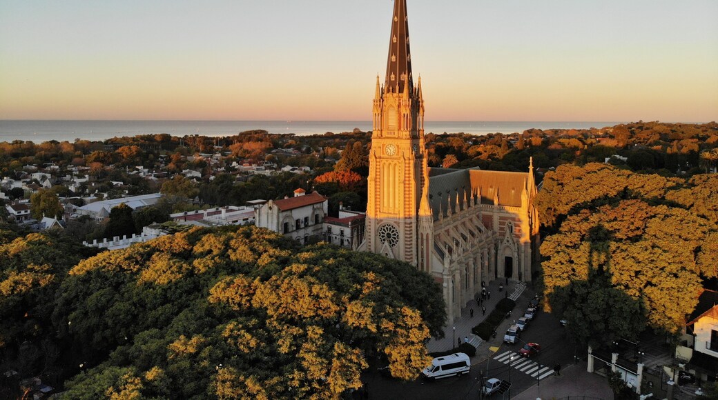 A cathedral with a tall spire, surrounded by trees and a coastal view.