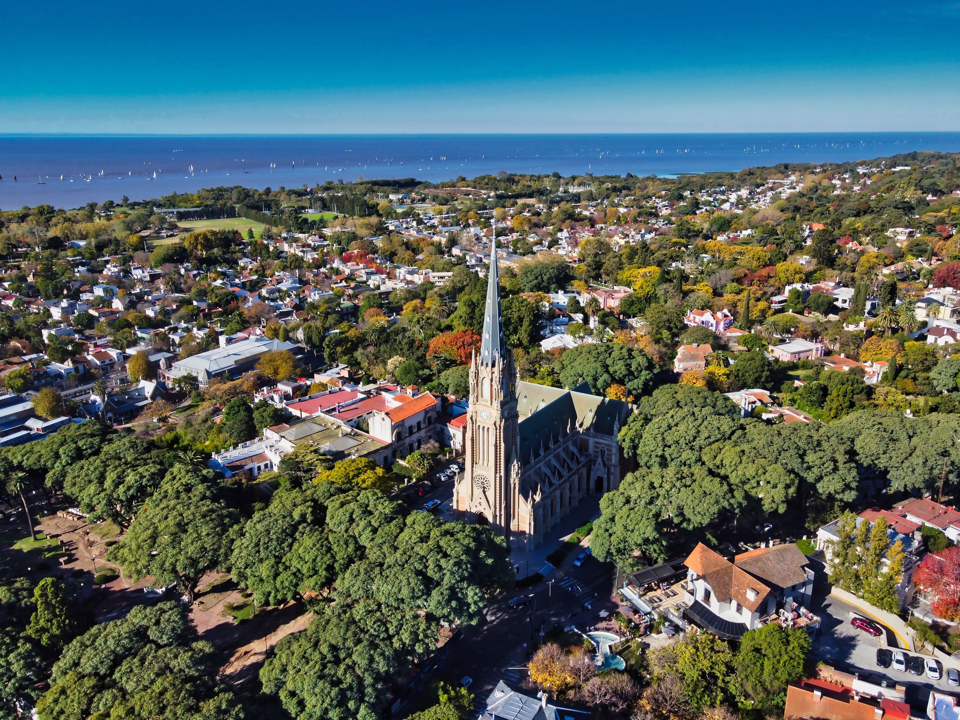 An aerial view of a coastal town with a prominent church spire, dense residential area, and a marina with sailboats.