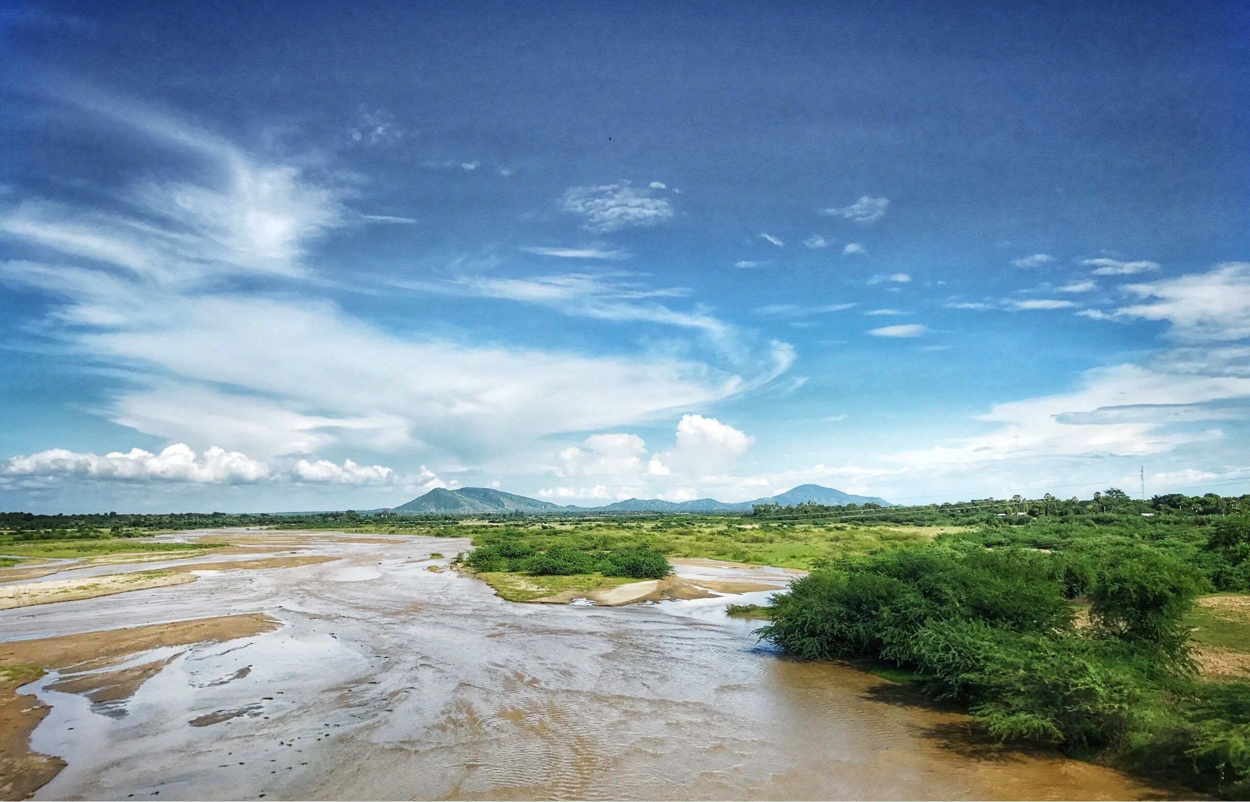 A river flowing through a green landscape with mountains in the background.
