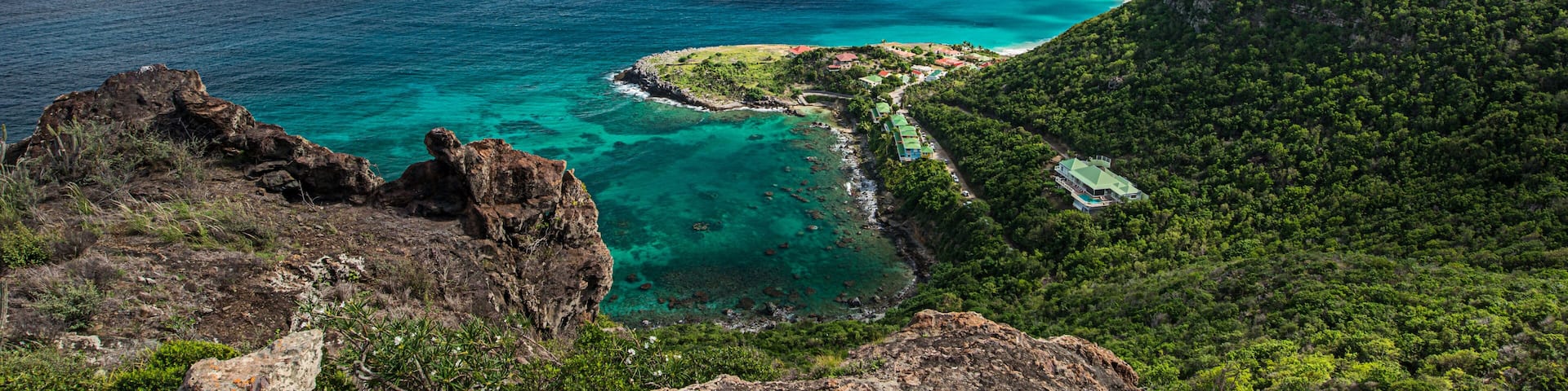 A coastal landscape with clear turquoise waters, rocky cliffs, and lush green hills.
