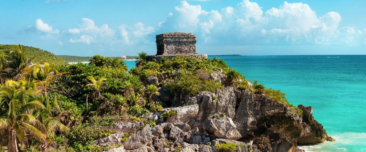 A coastal landscape with a stone structure on a cliff, turquoise waters, and lush greenery.