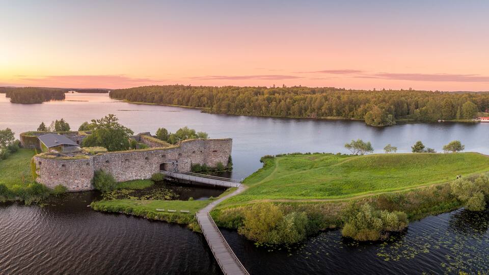 A historic fort on a grassy island surrounded by water, with a bridge connecting it to the mainland.