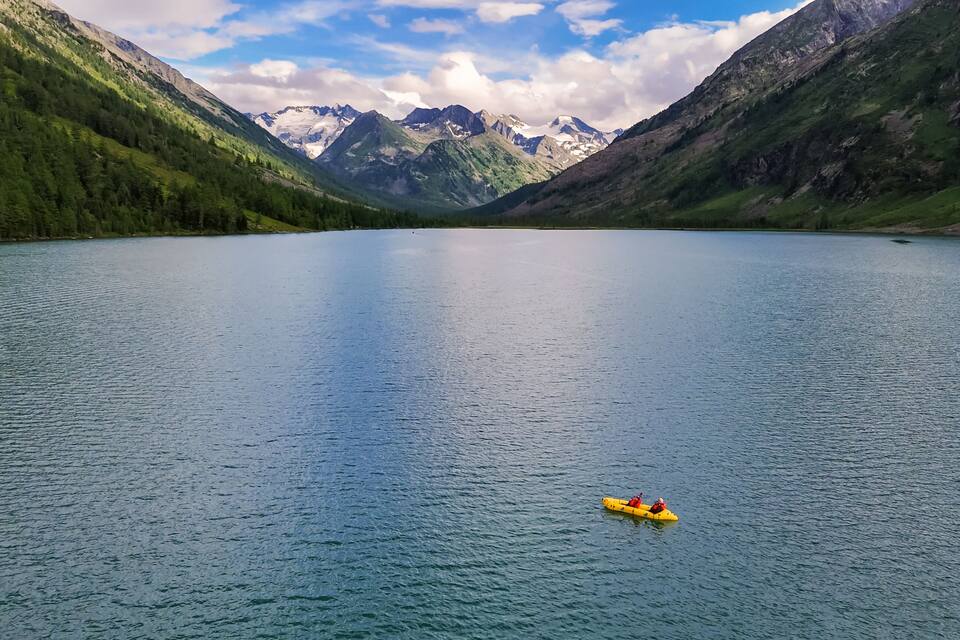 A calm lake surrounded by mountains with a yellow kayak in the water.