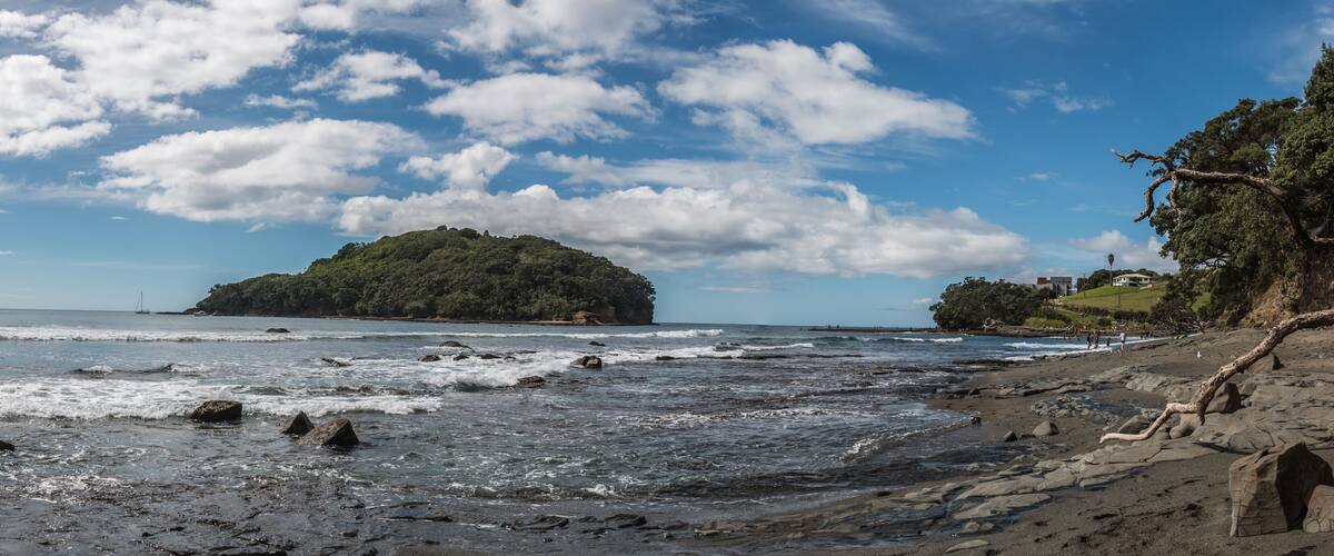 A rocky beach with waves, a small island, and a cliff with vegetation.