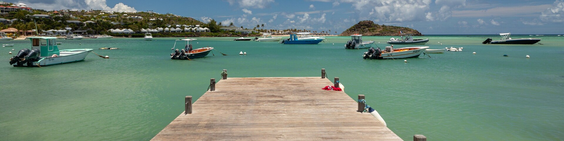 Un muelle de madera que se adentra en aguas turquesas, con varias embarcaciones amarradas.