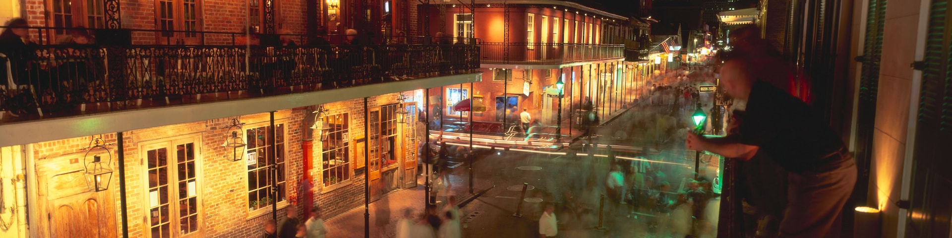 A nighttime street scene with brick buildings, a balcony, and a crowd of people.