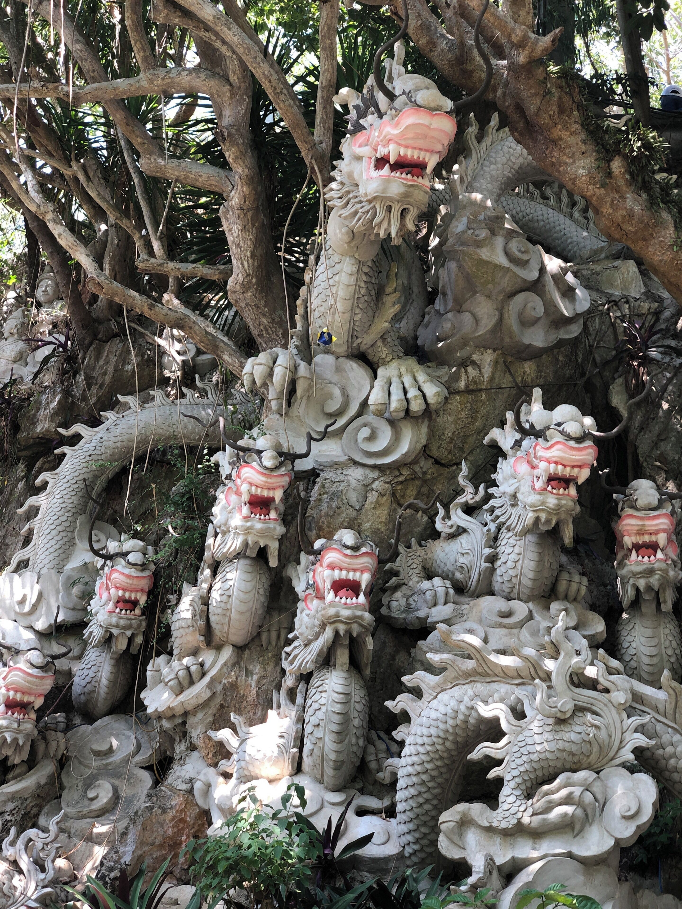 Escultura de un dragón de piedra con múltiples cabezas y un tronco de árbol grande al fondo.