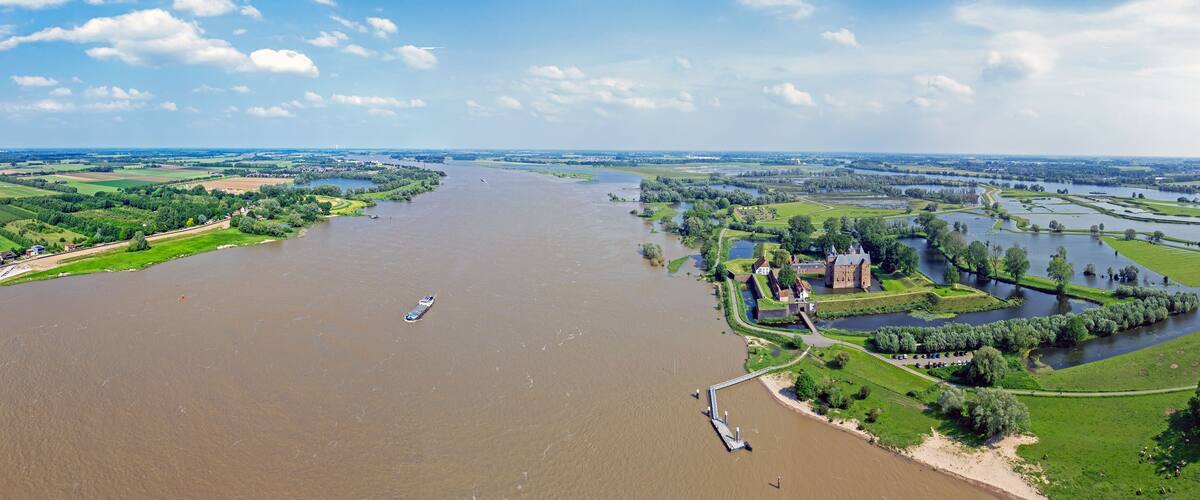 A river with a boat, surrounded by green fields and a castle.