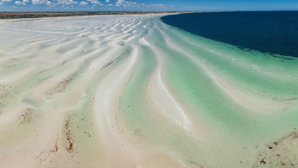 Panoramic view of white sand beach with ripples and pools of water in front alongside a blue ocean